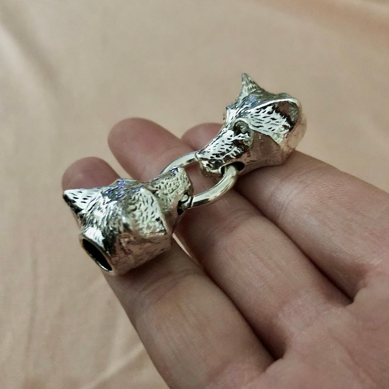 May include: Silver wolf head toggle clasp with a ring connecting two wolf heads. The heads are detailed with fur and have a realistic look.