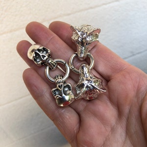 May include: A silver charm bracelet with three charms: a wolf head, a skull, and another wolf head. The charms are connected by silver rings.