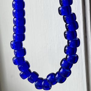May include: A necklace composed of vibrant, deep blue glass beads. The beads are rectangular with rounded edges, strung together to form a continuous loop. The necklace is displayed against a white background.