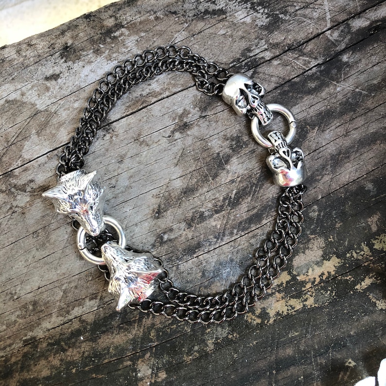 May include: A silver chain bracelet with two wolf head charms and a skull charm.