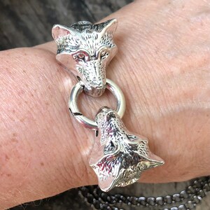 May include: Silver bracelet with two wolf head charms. The bracelet is made of a chain link design.