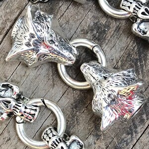May include: A silver chain bracelet with alternating wolf head and skull charms. The wolf heads are detailed with fur and have a realistic look. The skulls are simple and have a smooth finish.