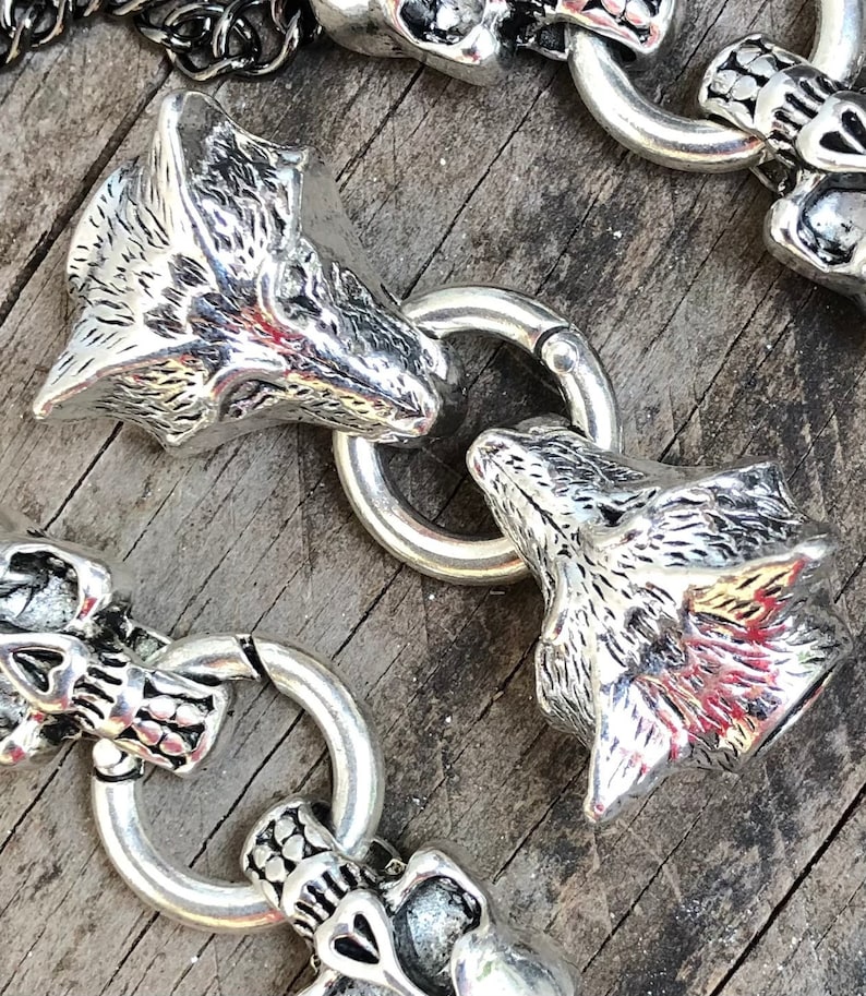 May include: A silver chain bracelet with alternating wolf head and skull charms. The wolf heads are detailed with fur and have a realistic look. The skulls are simple and have a smooth finish.