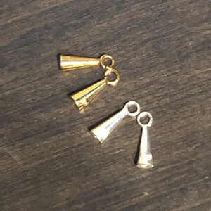 May include: Two sets of gold and silver metal cord end caps with loops. The cord end caps are shaped like cones.