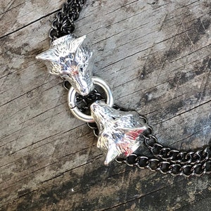 May include: A silver chain necklace with two wolf head pendants. The chain is black and silver and the wolf heads are detailed and realistic.