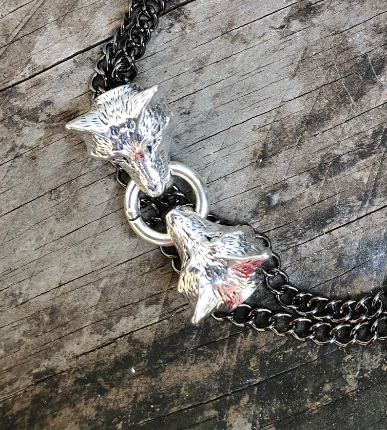 May include: A silver chain necklace with two wolf head pendants. The chain is black and silver and the wolf heads are detailed and realistic.