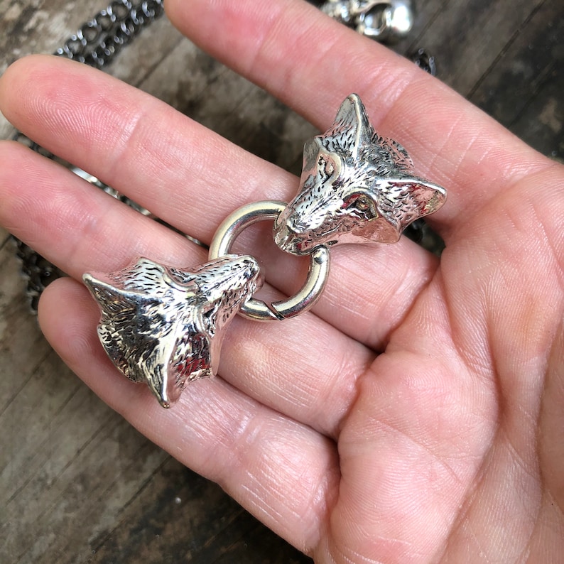 May include: A silver chain necklace with two wolf head charms. The charms are connected by a silver ring.