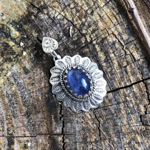 May include: A silver pendant with a blue gemstone set in a floral design.