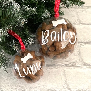May include: Two clear baubles filled with dog treats. Each bauble has a white bone graphic and a name in white script: "Bailey" and "Luna". Red and white polka dot ribbon hangs from the top of each bauble.