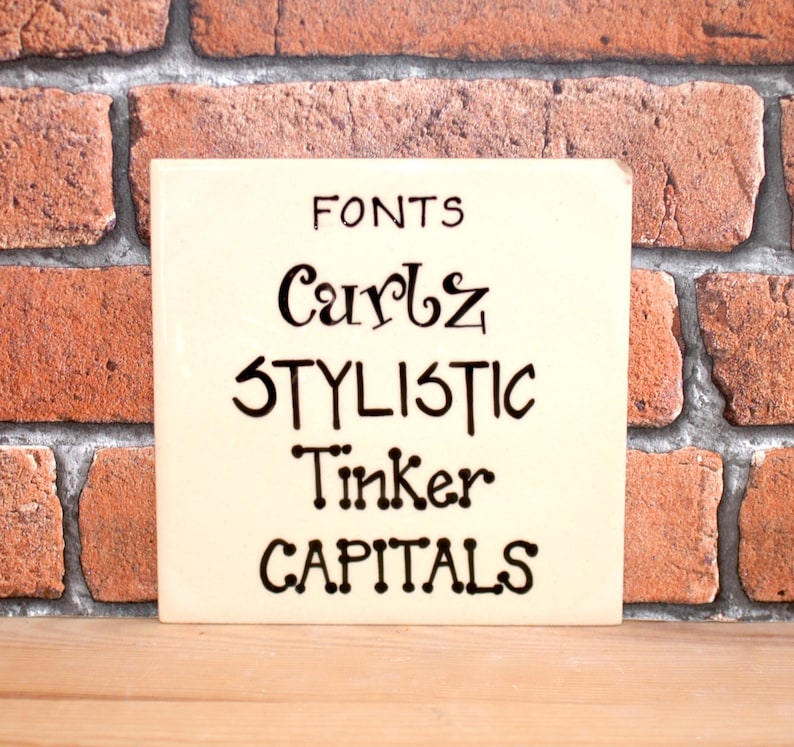 May include: A white ceramic tile with black lettering that reads "FONTS", "Curls", "STYLISTIC", "Tinker", and "CAPITALS".