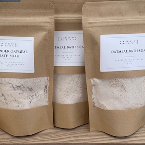 May include: Three brown paper bags with white labels. The labels have the text "7th Creations Rapid City, SD" and the names of the products: "Lavender Oatmeal Bath Soak", "Oatmeal Bath Soak", and "Oatmeal Bath Soak". The bags contain a white powder.