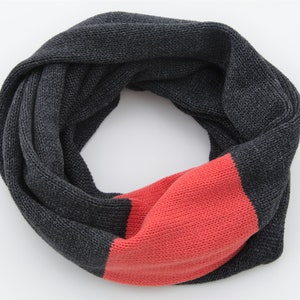 May include: A knitted infinity scarf in charcoal gray and coral red. The scarf is a continuous loop, with a section of coral red knit into the design. The scarf is made of a soft, textured yarn, perfect for cold weather.