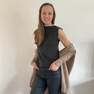May include: A woman wearing a black sleeveless top, black pants, and a beige cardigan. She is smiling and looking at the camera.