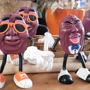 May include: A set of raisin figurines with human-like features. The raisins have arms, legs, and are wearing sunglasses, bow ties, and trainers. The figurines are in various poses, some with open mouths and others with arms outstretched.