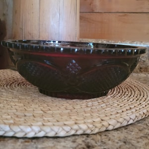 May include: A dark red glass bowl with a decorative pattern. The bowl is sitting on a woven placemat.