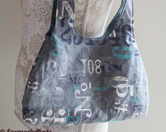 May include: A gray fabric tote bag with a teal and white graphic print of numbers and letters. The bag has a long teal strap.