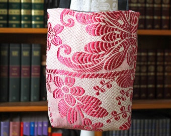 May include: A pink and white floral tote bag with black straps. The bag is made of a fabric with a woven pattern.