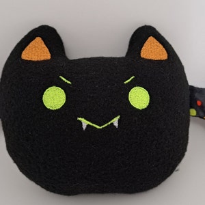 May include: A black plush bat with orange ears and candy corn patterned wings. The bat has green eyes and white fangs.