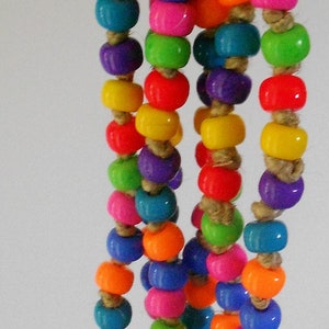 May include: A colorful bird toy featuring strands of vibrant, round beads in various colors, including orange, blue, pink, green, yellow, and purple. The beads are strung on natural twine and attached to a yellow and orange plastic hanging loop.