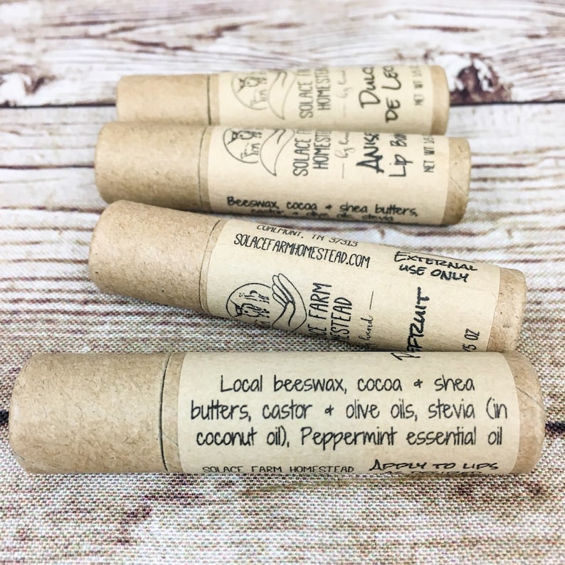May include: Four brown cardboard tubes with labels containing information about the lip balm products. The labels include the name of the product, ingredients, and instructions for use. The products are made by Solace Farm Homestead.