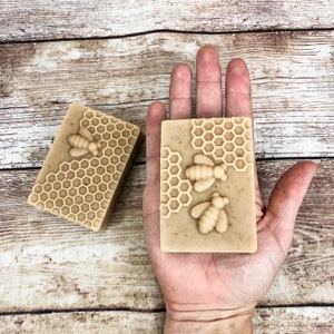 K&ouml;nnte beinhalten: Zwei handgemachte Seifenst&uuml;cke mit einem Waben- und Bienenmuster. Die Seife ist hellbraun und hat einen dezenten Honigduft.