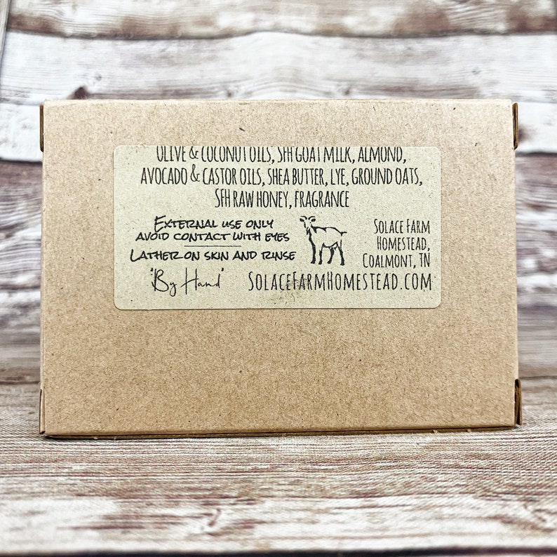 K&ouml;nnte beinhalten: Ein brauner Karton mit einem wei&szlig;en Etikett. Das Etikett listet die Zutaten des Produkts auf, darunter Oliven&ouml;l, Kokos&ouml;l, Sheabutter und Ziegenmilch. Das Etikett enth&auml;lt auch Gebrauchsanweisungen, wie z. B. den Kontakt mit den Augen zu vermeiden und auf der Haut einzusch&auml;umen. Das Etikett enth&auml;lt auch den Namen des Unternehmens, "Solace Farm Homestead", und die Website-Adresse.