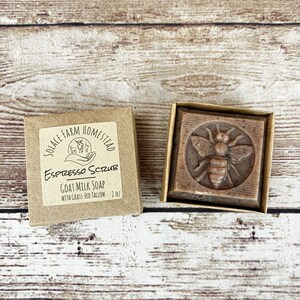 Puede incluir: Una caja de cart&oacute;n marr&oacute;n con una etiqueta blanca que dice "Solace Farm Homestead Espresso Scrub Goat Milk Soap with Grass-Fed Tallow 2.0z". La caja est&aacute; al lado de una caja de cart&oacute;n marr&oacute;n m&aacute;s peque&ntilde;a que contiene una barra de jab&oacute;n marr&oacute;n con un dise&ntilde;o de abeja.