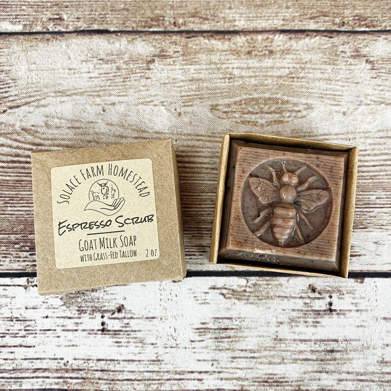 Puede incluir: Una caja de cart&oacute;n marr&oacute;n con una etiqueta blanca que dice "Solace Farm Homestead Espresso Scrub Goat Milk Soap with Grass-Fed Tallow 2.0z". La caja est&aacute; al lado de una caja de cart&oacute;n marr&oacute;n m&aacute;s peque&ntilde;a que contiene una barra de jab&oacute;n marr&oacute;n con un dise&ntilde;o de abeja.