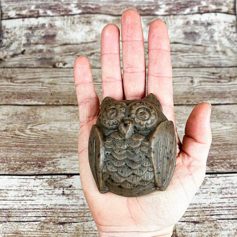 Puede incluir: Una pastilla de jab&oacute;n en forma de b&uacute;ho marr&oacute;n y negro con detalles elaborados. El jab&oacute;n est&aacute; sentado en la palma de una mano.