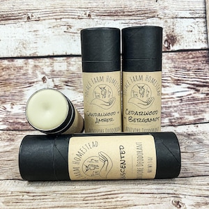 May include: Three black and brown cardboard tubes with white labels. The labels have a hand holding a small animal and the text "Solace Farm Homestead". The tubes contain natural deodorant with the scents "Sandalwood + Amber", "Cedarwood + Bergamot", and "Unscented".