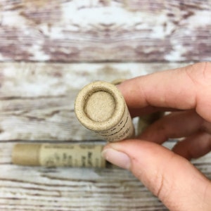 May include: Close-up of the top of a cardboard tube with a brown paper lid. The tube is partially visible and has text on it.