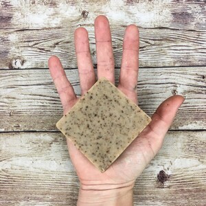Puede incluir: Una pastilla de jab&oacute;n cuadrada de color marr&oacute;n y beige moteado. El jab&oacute;n est&aacute; en la palma de una mano.