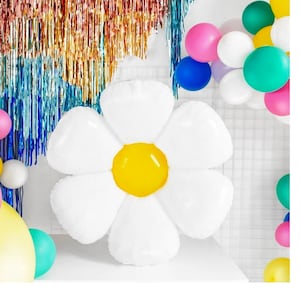 May include: A large white inflatable daisy flower with a yellow center. The flower is surrounded by colorful balloons.