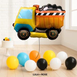 May include: A yellow and blue dump truck-shaped balloon with black wheels and an orange cargo bed. The balloon is accompanied by several colorful balloons in yellow, blue, orange, white, and black. The text "LULA + ROSE" is at the bottom.