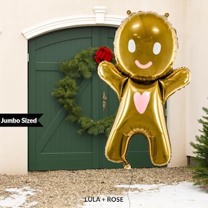 May include: A jumbo-sized gold gingerbread man balloon with a pink heart and facial features. The balloon is in front of a green door with a Christmas wreath and the text "LULA + ROSE".