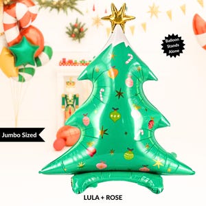 Puede incluir: Globo gigante con forma de árbol de Navidad verde, con detalles blancos y una estrella dorada. Decorado con adornos y bastones de caramelo. El globo se mantiene de pie solo. El texto en el globo dice "LULA + ROSE".