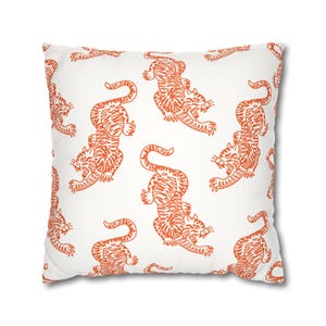 May include: Square white throw pillow with a repeating pattern of orange tigers. The tigers are depicted in a stylized, illustrative style, with their bodies in various dynamic poses. The pillow has a clean, modern aesthetic.