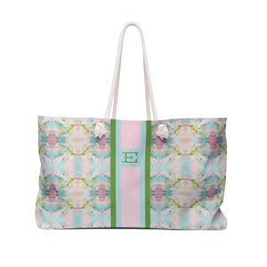 Könnte beinhalten: Große Tragetasche mit einem farbenfrohen abstrakten Muster in Rosa, Blau und Grün. Die Tasche hat weiße Seilgriffe und einen vertikalen Mittelstreifen in Rosa und Hellblau, mit grünem Rand und einem monogrammierten Buchstaben "E".
