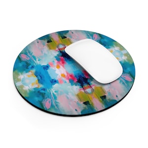 May include: Round mouse pad with an abstract design featuring bright colors like blue, pink, yellow, and white. The mouse pad has a black border.