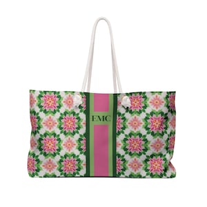 May include: Large tote bag with a floral pattern in pink, green, and white. The bag has a vertical pink stripe with the initials "EMC" in the center. It features white rope handles and is designed for carrying items.