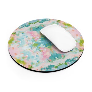 May include: A round mouse pad with a colorful abstract design in shades of pink, blue, and green. A white computer mouse is sitting on the pad.