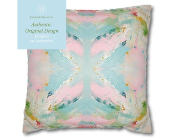 May include: A square throw pillow featuring an abstract painterly design with blended pastel shades of light blue, soft pink, white, and touches of gold. The surface displays textured brushstrokes in a symmetrical pattern across the fabric.