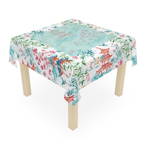 May include: A white tablecloth with a colorful Japanese-inspired design featuring pagodas, cherry blossoms, and bamboo. The tablecloth is draped over a wooden table with four legs.