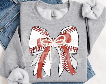 May include: A heather gray crewneck sweatshirt featuring a large graphic of a white bow with red baseball-style stitching and a string of white pearls draped across the center. The sweatshirt is layered over blue denim jeans.