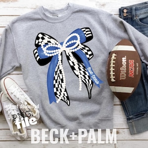 May include: A gray sweatshirt featuring a large bow design with blue and black checkered patterns, accented with a string of pearls. The bow has blue ribbons with the text "Blue Devils". A football and white sneakers are also in the image.