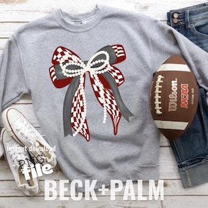 Op de afbeelding: Een grijze sweatshirt met een groot strikdesign met rood-witte geblokte linten, grijze linten en een parelsnoer. Een bruine voetbal en witte sneakers zijn ook zichtbaar. De tekst "BECK+PALM" staat onderaan.