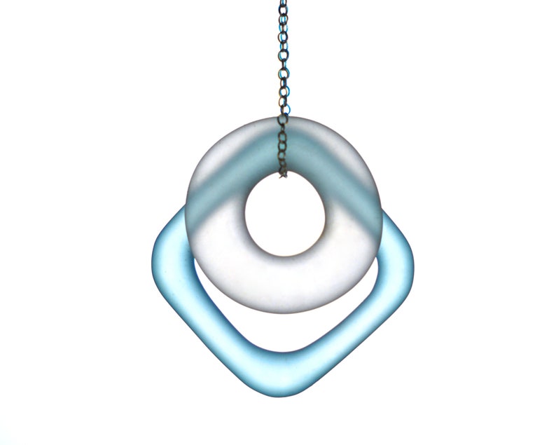 May include: A silver chain hangs from a light blue glass ring with a larger, frosted glass ring inside. The rings are suspended from a silver chain.