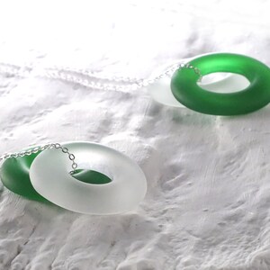 May include: A silver chain necklace with two glass rings. One ring is green and the other is white.