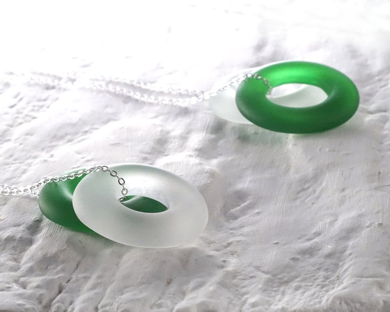 May include: A silver chain necklace with two glass rings. One ring is green and the other is white.