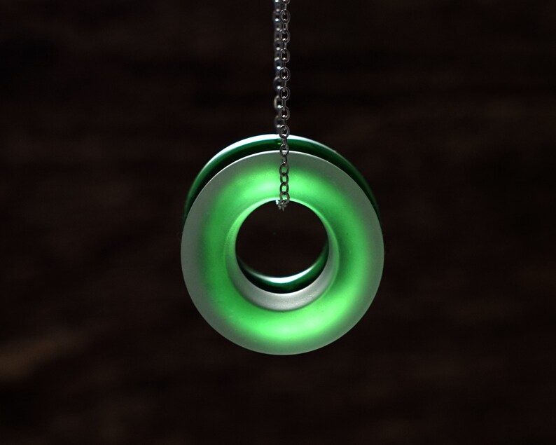 May include: A green glass pendant with a silver chain. The pendant is a double ring with a hollow center.
